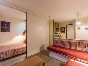 Una habitación compacta con cama, un banco, una pequeña mesa y una kitchenette.