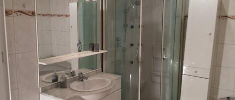 A modern bathroom with a curved glass shower enclosure, a sink with a mirror, and a toilet.