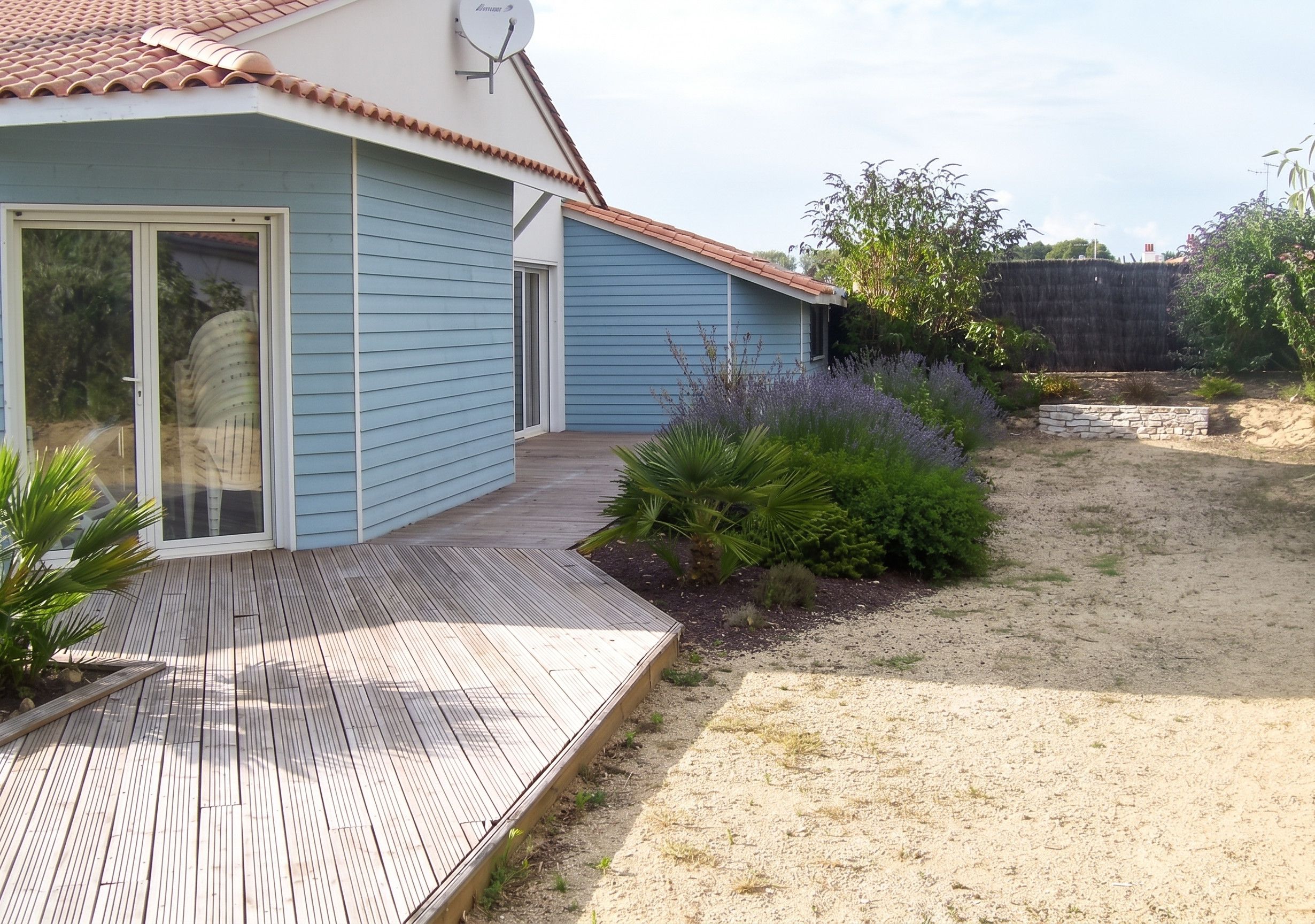 Ein Haus mit blauer Fassade, einem Ziegeldach und einer Holzterrasse.