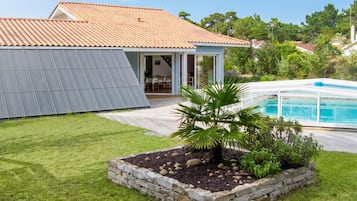 Une maison avec un toit en tuiles, une piscine et un jardin agrémenté d’un palmier.