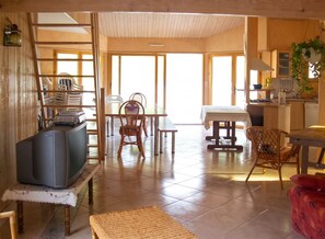 A spacious living area with a television, dining table, chairs, and a kitchen area with a stove and sink. - Homerez - Villa in Saint Hilaire de Riez (Saint Hilaire de Riez)