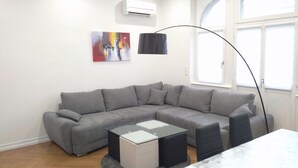 Ein modernes Wohnzimmer mit einem grauen Ecksofa, einem kleinen weißen Couchtisch und einer schwarzen Stehlampe.