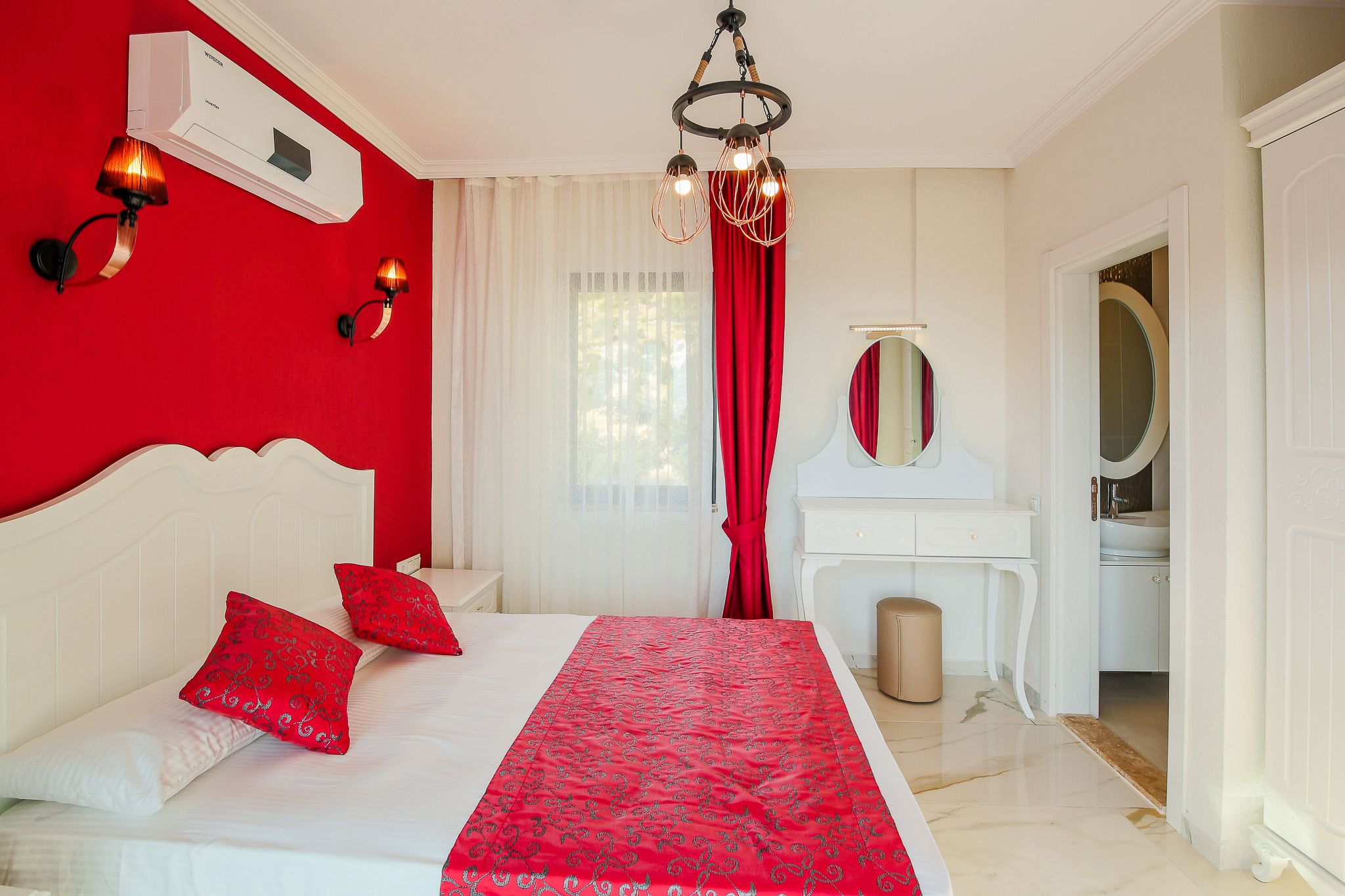 A bedroom with a white bed, red bedding, a white dresser, and a mirror.