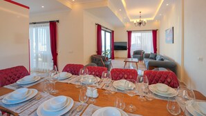 Un coin repas avec une table en bois dressée pour le repas, des chaises à revêtement rouge, et un coin salon avec un canapé et un téléviseur.