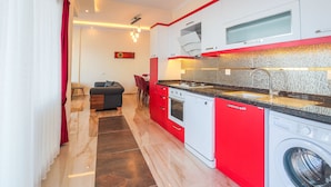 Une cuisine moderne avec des meubles de rangement rouges et blancs, un four encastré, un lave-linge et un coin repas comprenant une table et des chaises.