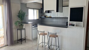 Een moderne keuken met een inbouwfornuis, een spoelbak en een aanrecht. Twee barkrukken en een potplant staan er.