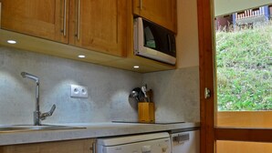 Una cucina compatta con mobili in legno, forno a microonde integrato, lavello con rubinetteria e lavastoviglie.