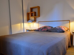A neatly made bed with a wooden headboard, a bedside table with a lamp, and a wall-mounted shelf.