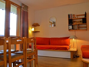 Ein gemütliches Wohnzimmer mit einem Holzsofa, einem Holzstuhl, einer Lampe und einem Bücherregal.