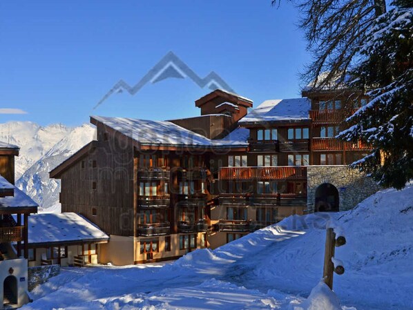 A multi-story wooden building with balconies and a ski slope in the background.