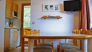 Cucina compatta con mobili in legno, forno a microonde e frigorifero. C'è un tavolo da pranzo con quattro sedie e una TV a schermo piatto montata a parete.