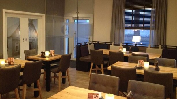 A restaurant with wooden tables and chairs, a glass partition, and a view of the outside. - Köhncke's Landgasthof und Hotel (Wiefelstede)