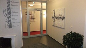 A hallway with a reception desk, a wall-mounted sign with multiple languages, a glass door, and a painting. - Köhncke's Landgasthof und Hotel (Wiefelstede)
