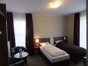 A hotel room with two single beds, a small table with a chair, a nightstand, and a window with curtains. - Köhncke's Landgasthof und Hotel (Wiefelstede)