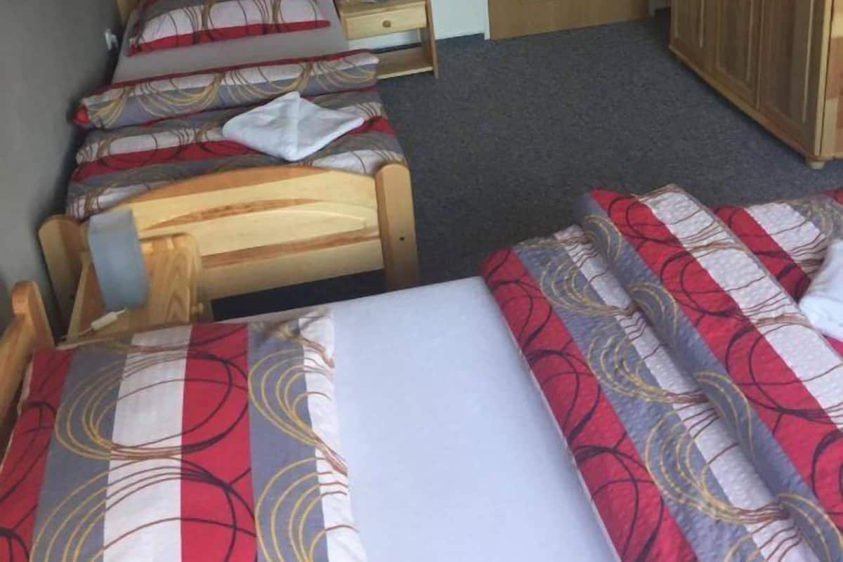 Una habitación con tres camas de madera, cada una con ropa de cama estampada. Se ve un armario de madera y una puerta al fondo.