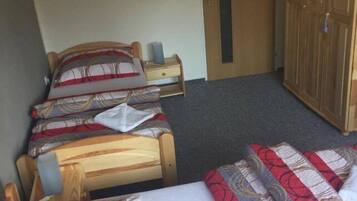 Ein Zimmer mit drei hölzernen Betten, jedes mit gemusterten Bettbezügen. Im Hintergrund steht ein Holzschrank und eine Tür.