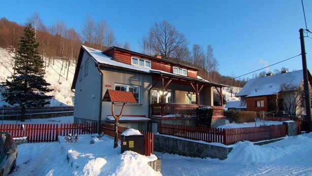 Ein zweigeschossiges Haus mit rotem Dach, einer Veranda und einer Steinmauer.