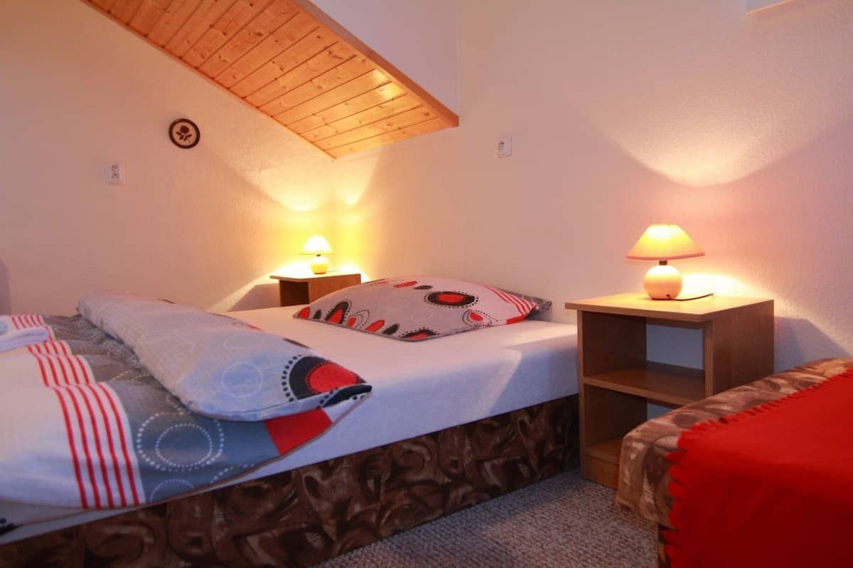 Un dormitorio con cama tipo altillo, dos mesitas de noche con lámparas, una manta roja y una colcha estampada.
