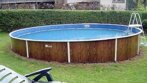 Ein oberirdischer Pool mit Holzverkleidung, umgeben von einer Rasenfläche und einem Heckenstreifen.