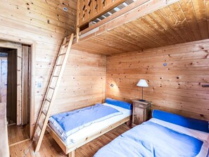 A cabin with two wooden bunk beds, a ladder, a small bedside table with a lamp, and a door leading outside.