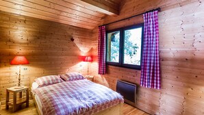 Quarto de cabana de madeira com uma cama, duas luminárias de cabeceira, uma janela com cortinas e um radiador.