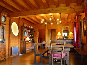 Cozy cabin interior with a wooden dining table, bookshelf, and chandelier.