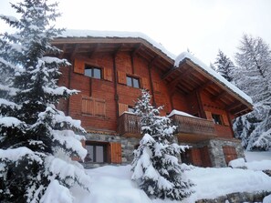 A wooden chalet with a stone foundation, wooden balconies, and snow-covered trees. - Chalet spacieux, 3 niveaux, 10 personnes, 4 chambres, proche pistes et centre, Wi-Fi, parking gratuit. (Bellentre)
