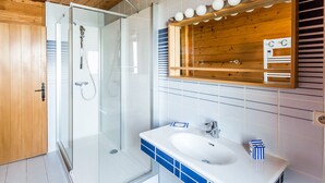 Uma casa de banho moderna com cabine de duche em vidro, teto de madeira e lavatório branco com azulejos azuis.