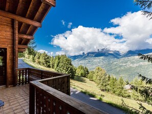 A wooden balcony with a view of a mountain range and a clear blue sky.