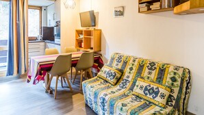 Uma sala de estar aconchegante com um sofá, uma mesa de jantar com cadeiras, uma televisão e uma estante de livros.