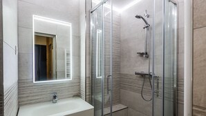 Um banheiro moderno com chuveiro em gabinete de vidro, toucador com espelho e piso revestido de azulejos.