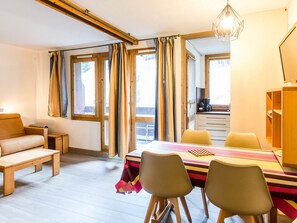 A cozy room with a wooden bench, a table with chairs, a desk, and a view through large windows.