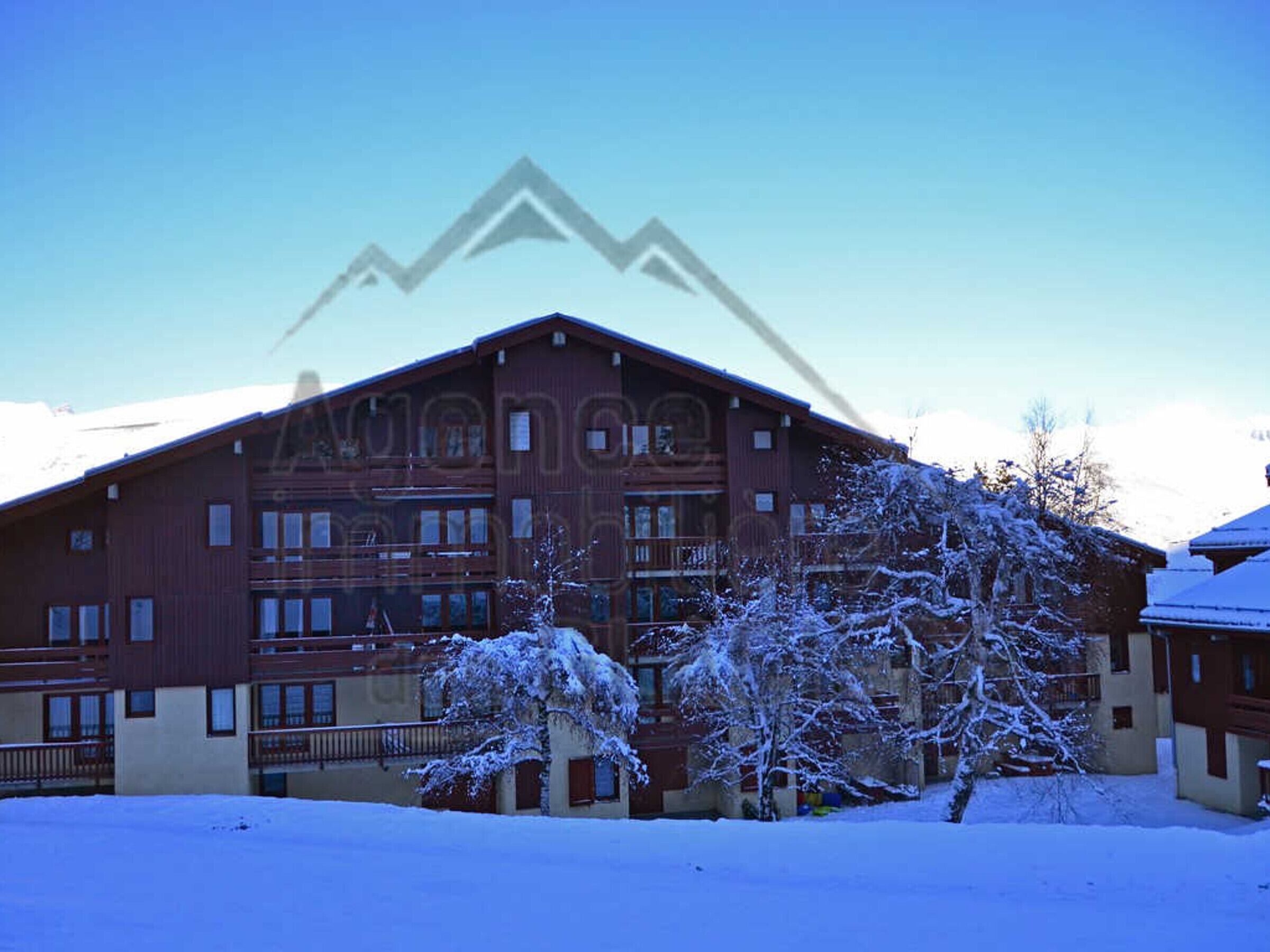 A multi-story building with a red facade and balconies, surrounded by snow-covered trees.