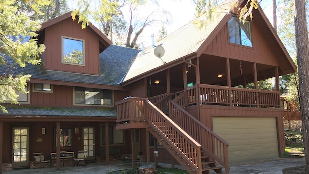 Une cabane à deux étages avec une véranda couverte, un escalier et un garage.