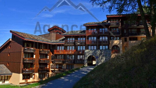 A multi-story hotel with a stone facade, wooden balconies, and a clear sky.