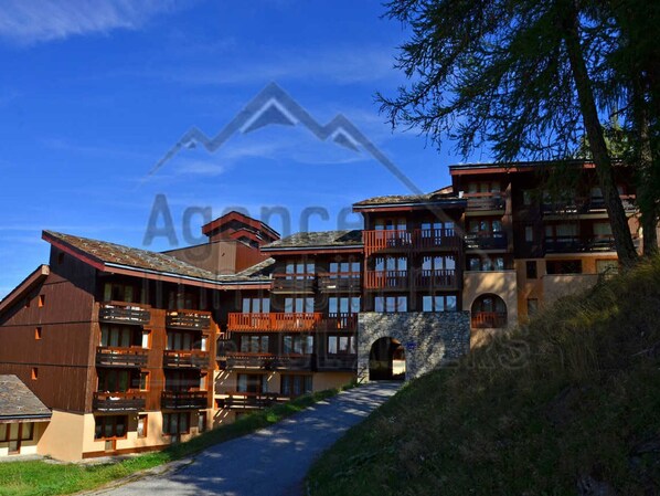 A multi-story hotel with a stone facade, wooden balconies, and a clear sky.