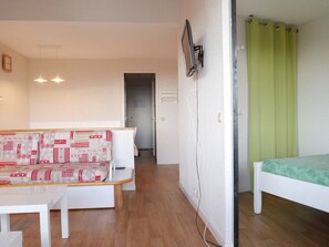 A room with a white sofa, a bed with a green bedspread, a white table, and a green curtain.