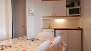 A compact kitchen with white cabinets, a dishwasher, and a small countertop. There is a dining table with chairs and a patterned tablecloth.
