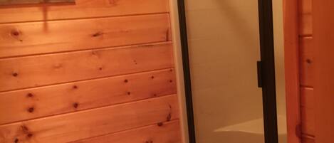 A wooden cabin with a glass door leading to a shower area.