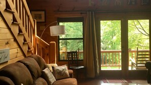 Interior de una cabaña de madera con sofá, una mesa de comedor y una escalera.
