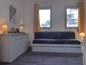 Un dormitorio con cama, cómoda, lámpara de pared y ventana con cortinas.
