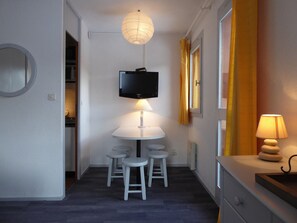 A compact room with a round table, four stools, a television mounted above the table, and a lamp on the right side.