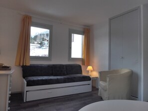 A room with a bed, a chair, a lamp, and a view of a snowy landscape through two windows.