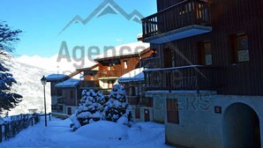 A snow-covered building with a balcony, a snow-covered tree, and a mountain in the background. - Divisible studio near slopes, 4 pers., parking, nice view (Bellentre)
