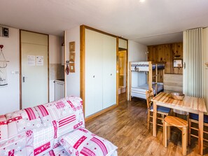 Una habitación compacta con literas, un pequeño rincón americano y un sofá con un estampado decorativo.