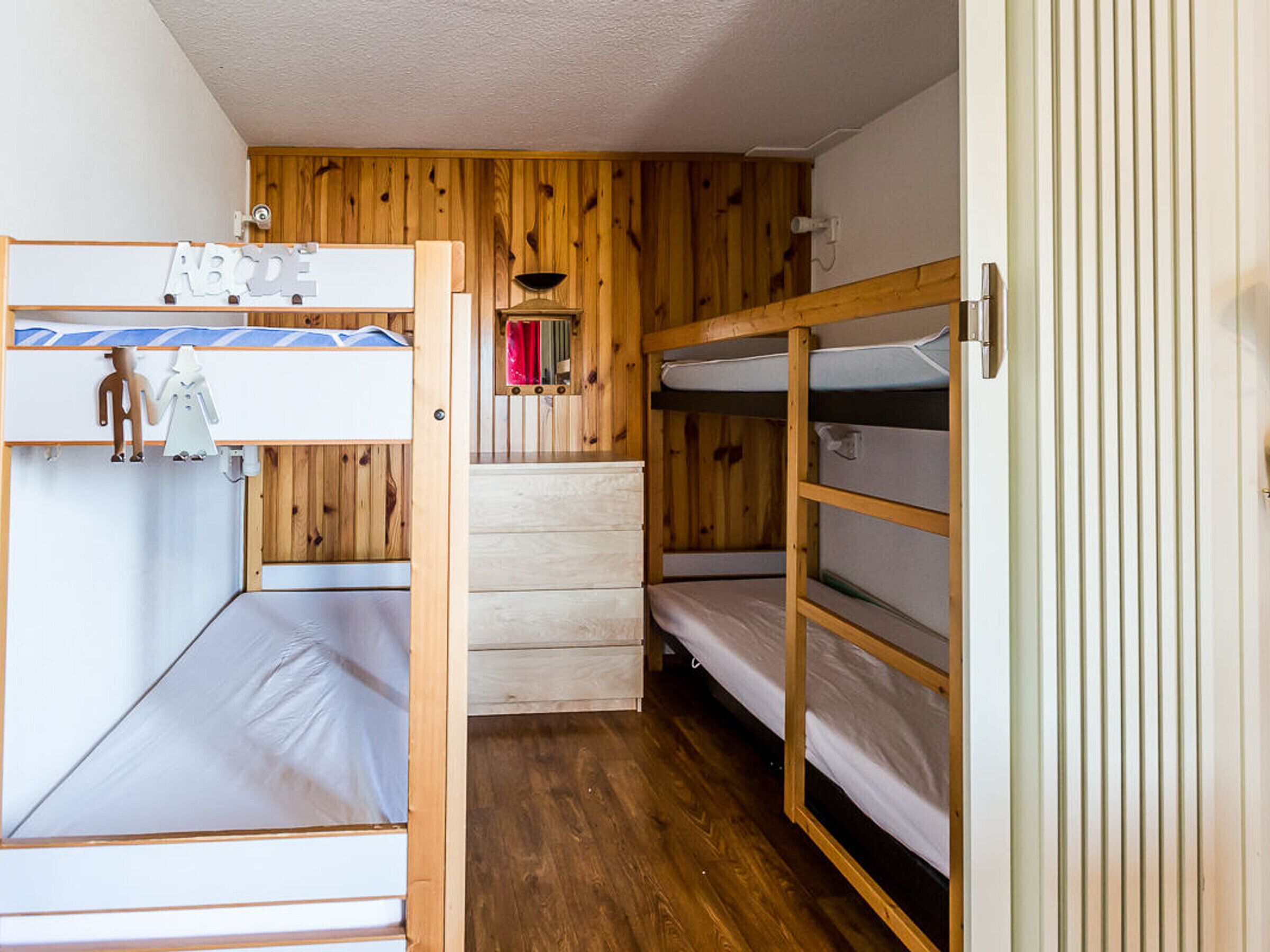 Une chambre avec des lits superposés, des murs en bois et une petite étagère avec des lettres de l’alphabet.