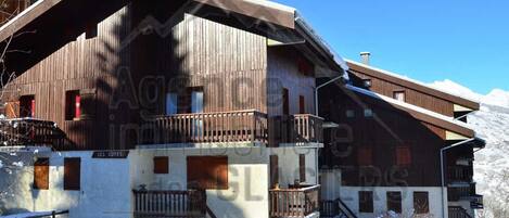 A chalet-style building with a wooden exterior, a balcony, and a staircase leading to the entrance.