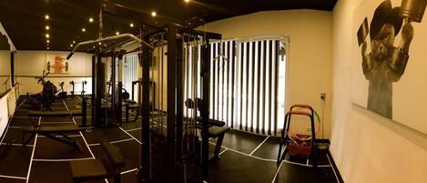 Een sportschool met trainingsapparatuur, spiegels en een groot schilderij aan de muur.