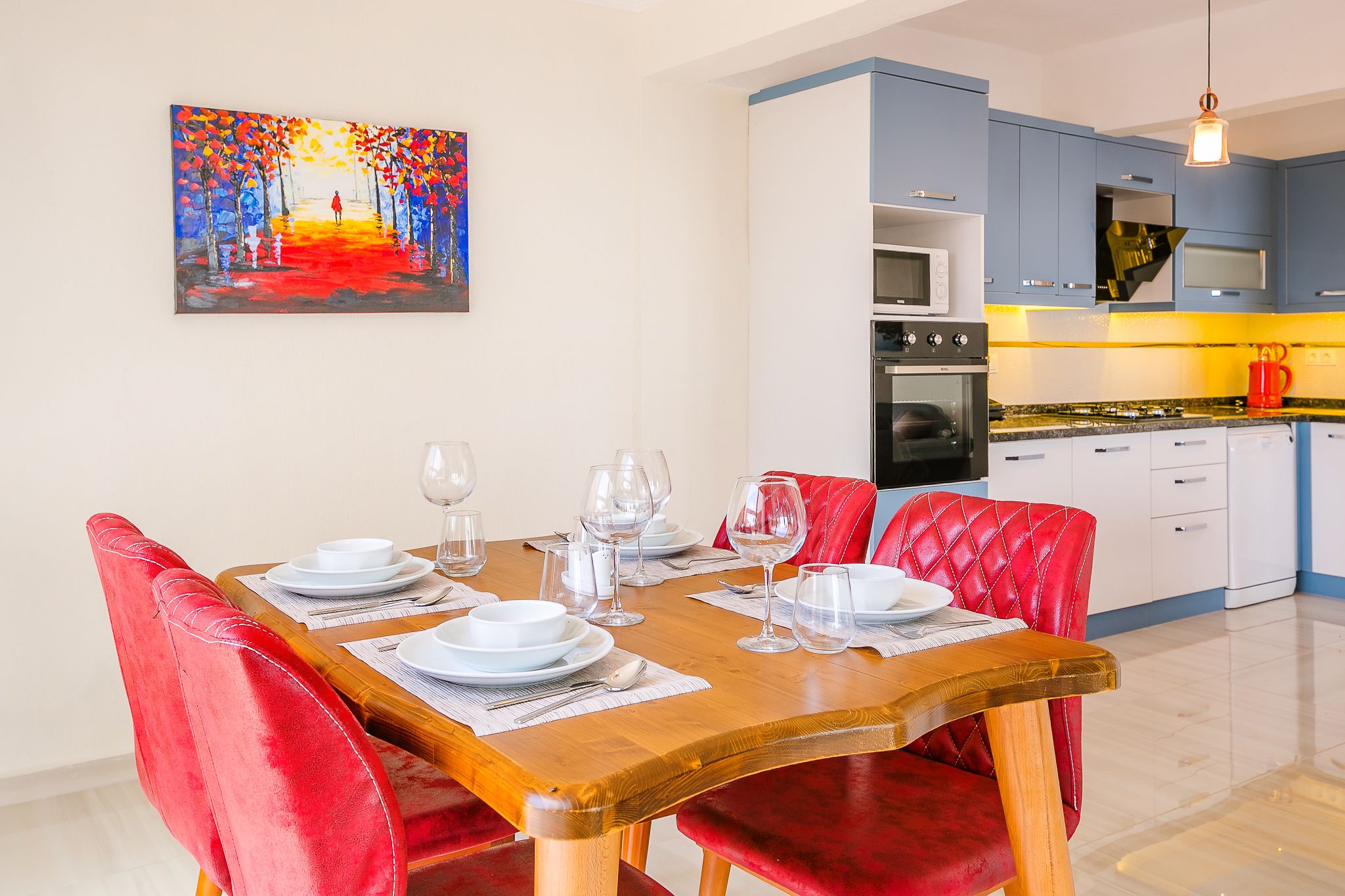 A dining area with a wooden table set for six, red upholstered chairs, and a painting above the table.