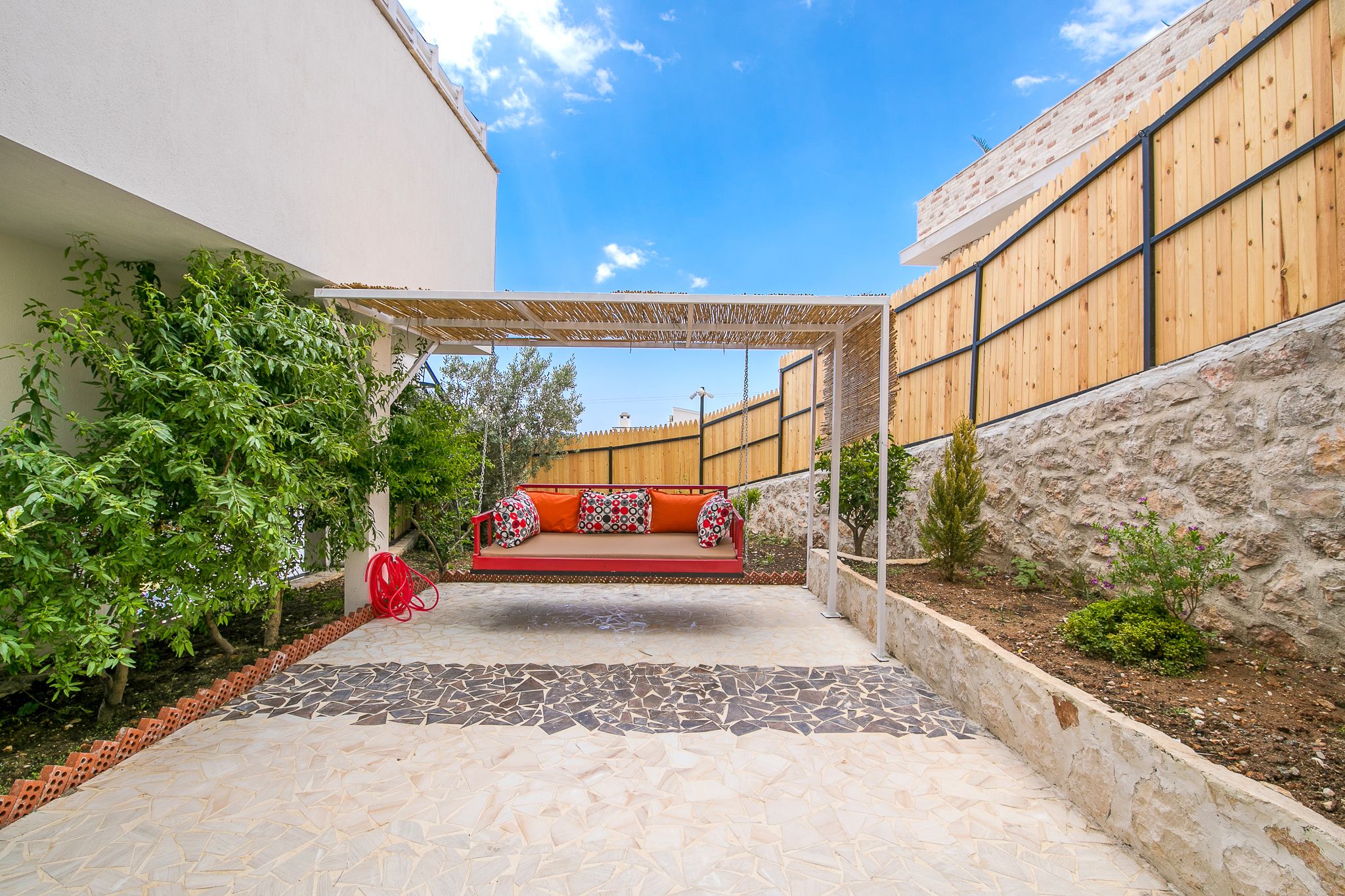 Un patio con un sofá rojo, una pérgola y un suelo de baldosas de piedra.